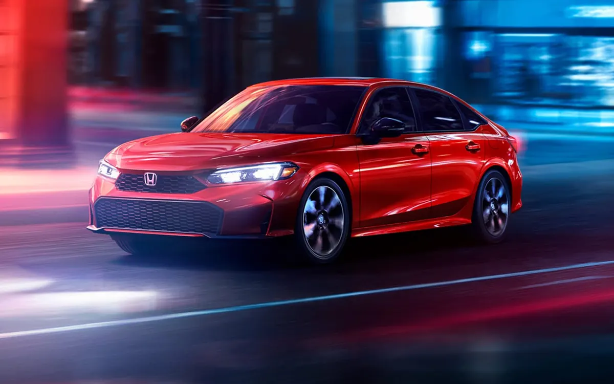 2027 Honda Civic sedan in red driving on a city street at night