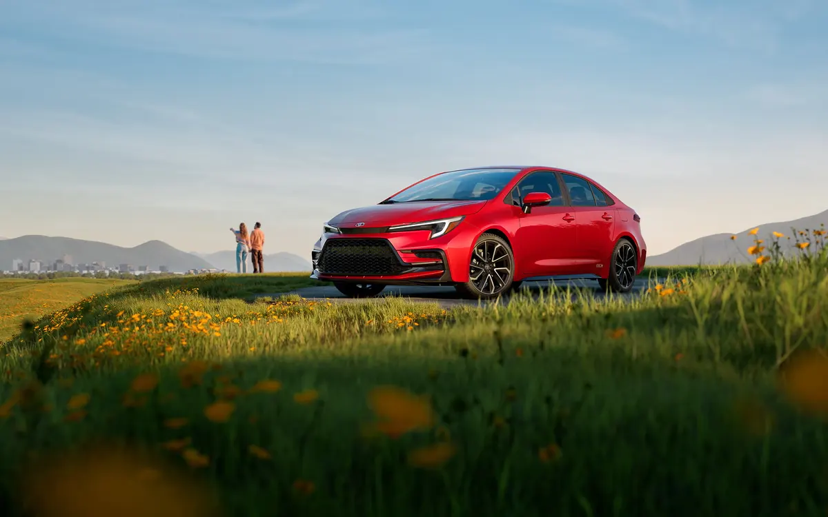 2027 Toyota Corolla sedan in red, front three-quarter view, parked on a grassy hillside